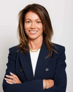 Headshot_Caitriona_01 Smiling businesswoman with arms crossed, wearing a navy blazer and gold jewelry.