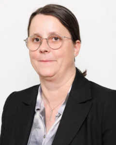 Headshot_Pascale_01 Professional headshot of a woman with round glasses, wearing a black blazer and light blouse against a neutral background.