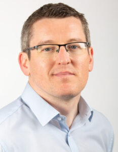 Stephen-photo-for-web Professional head-and-shoulders portrait of a man wearing glasses and a light blue button-down shirt against a neutral background, looking at the camera with a slight smile.